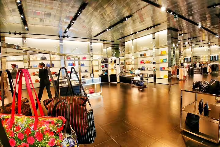 Spacious designer outlet interior at The Mall Tuscany, filled with luxury handbags, fashion racks and modern mirrored decor
