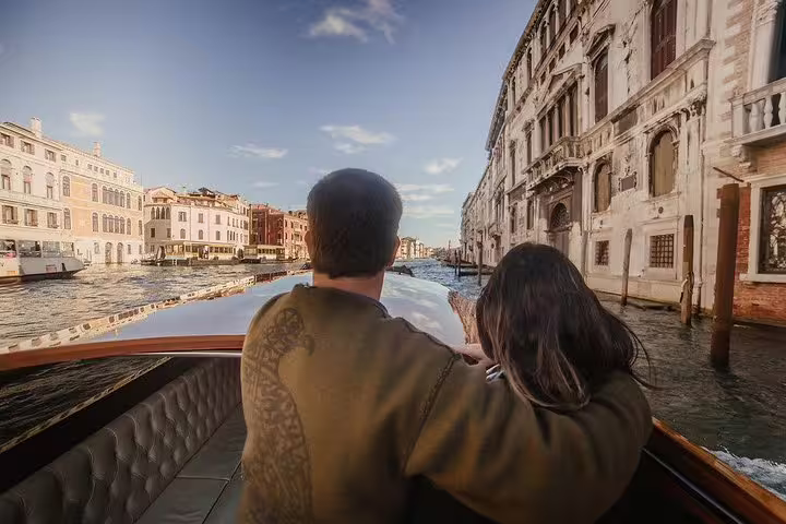 Couple enjoying a luxurious gondola ride on Venice's Grand Canal, surrounded by historic architecture and sunny skies.