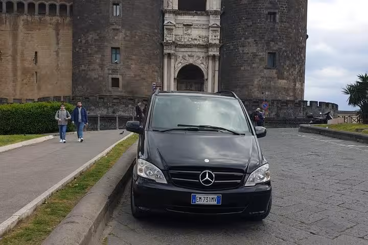 Luxury black Mercedes van parked in front of historic Naples castle, ideal for private transfers to Positano.