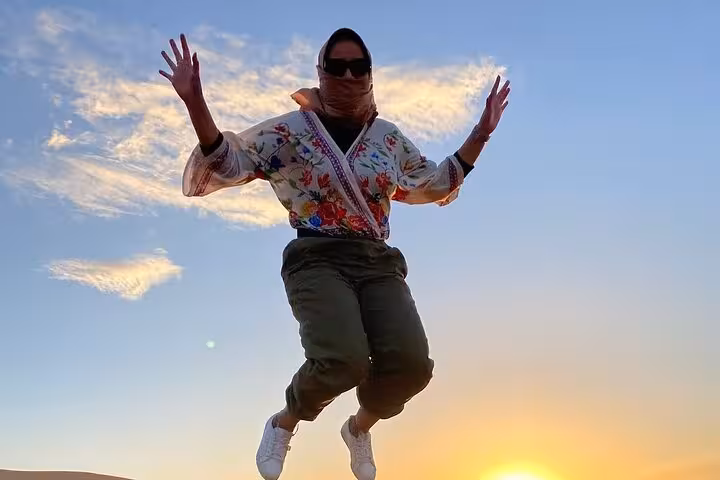 Traveler joyfully jumping against a vibrant sunset in the Moroccan desert, showcasing adventure on a luxury tour from Fes.