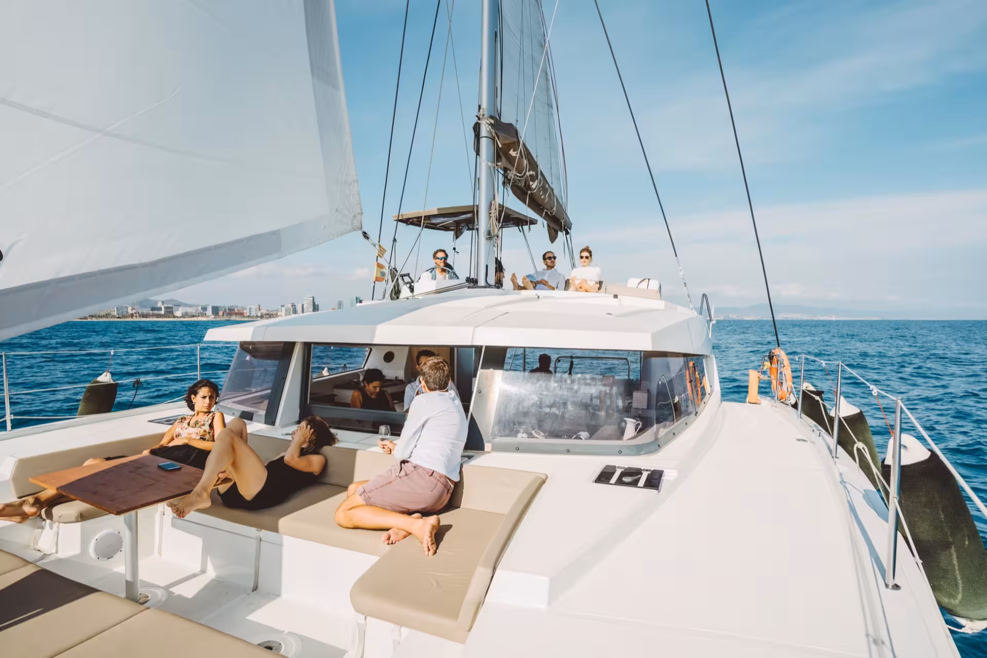 Guests relax on a luxury private catamaran rental deck with sun pads, sailing on calm blue sea