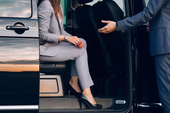 Professional chauffeur assisting a businesswoman into a luxury vehicle for a private transfer service.