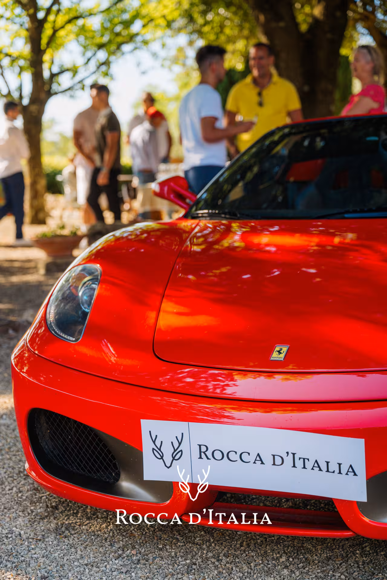 Luxury red supercar with a group of people enjoying a sunny day in the picturesque Tuscany landscape.