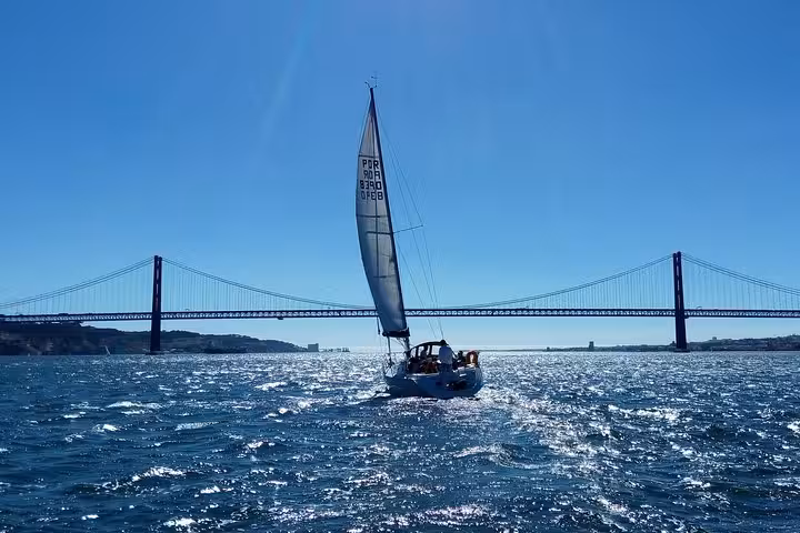 Luxury sailing yacht cruising under Lisbon’s 25 de Abril Bridge on Tagus River, with 2 drinks included