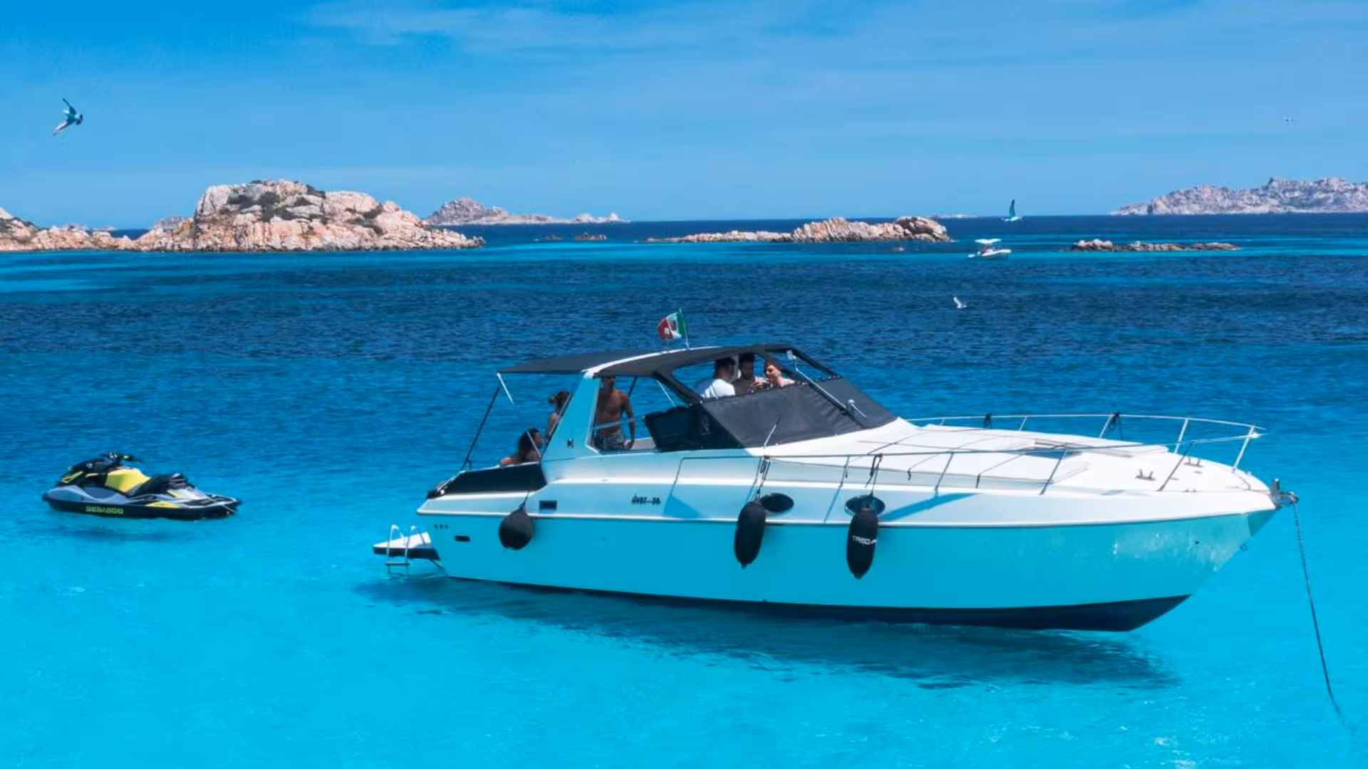 Luxury boat anchored in clear blue waters of La Maddalena Archipelago with scenic rocky islands in the background.