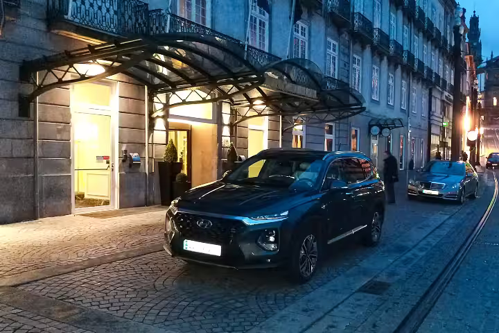 Luxury SUV parked outside a grand hotel at dusk, promoting premium private chauffeur and executive car hire service.