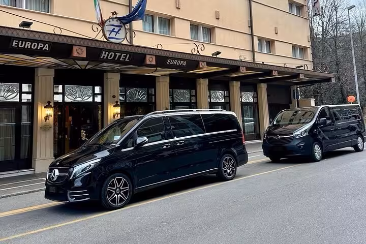 Luxury vans parked outside Europa Hotel for small group tour with lunch including Lamborghini, Ferrari, and gourmet tastings.