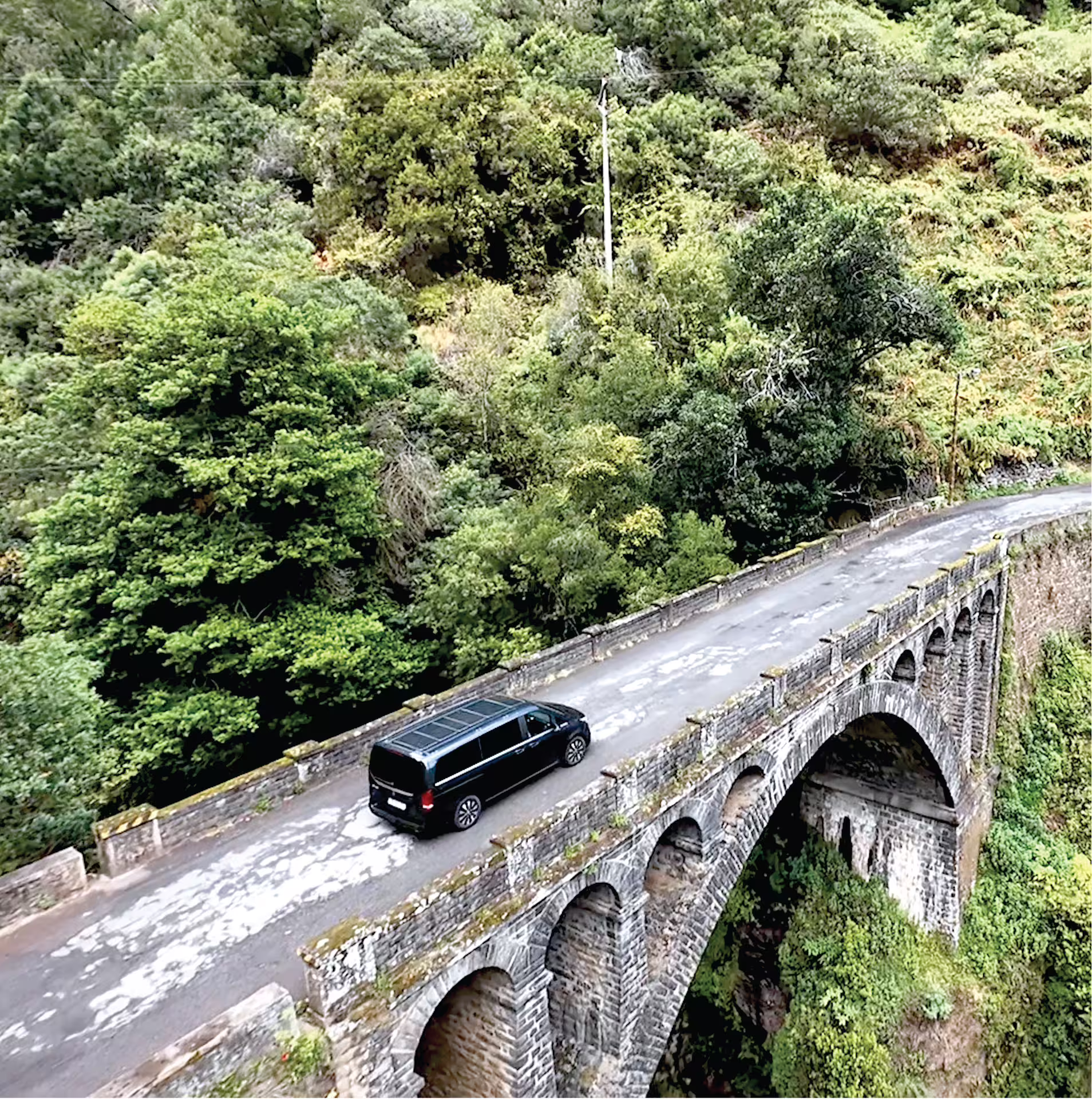 Luxury van crossing a scenic stone bridge surrounded by lush greenery on a private Madeira tour tailored for comfort and exploration.