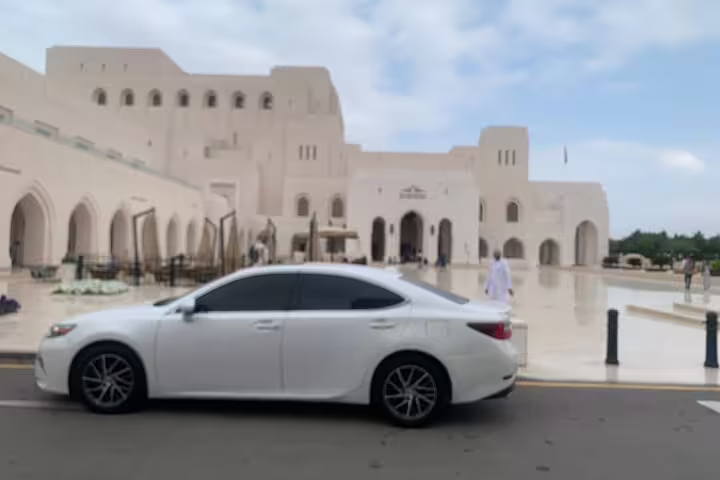 Luxury white car parked outside the stunning Sultan Qaboos Grand Mosque in Muscat, perfect for a private tour.