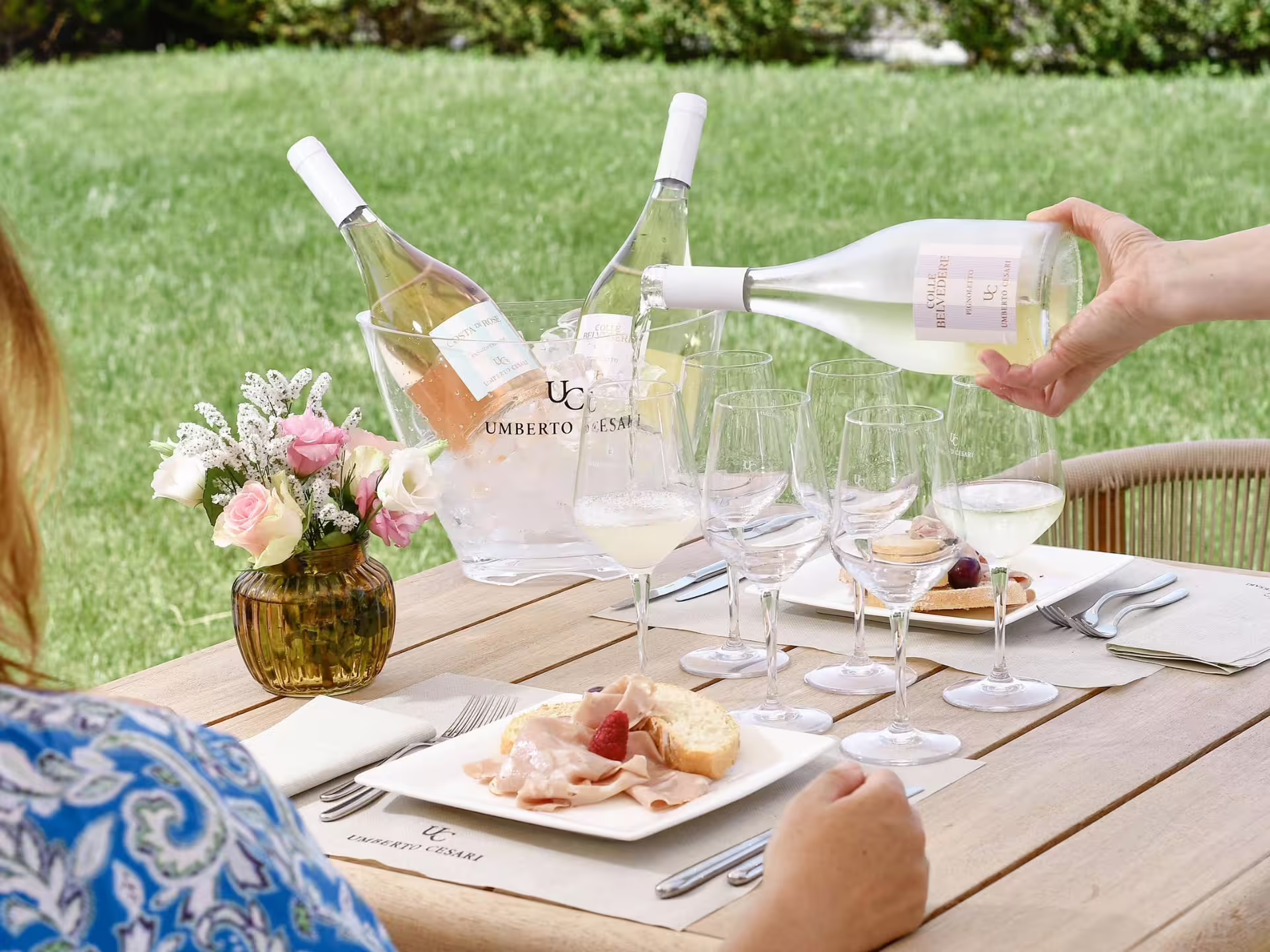 Outdoor wine tasting setup with white wine and gourmet food pairing near Bologna, featuring fresh flowers and elegant glasses.