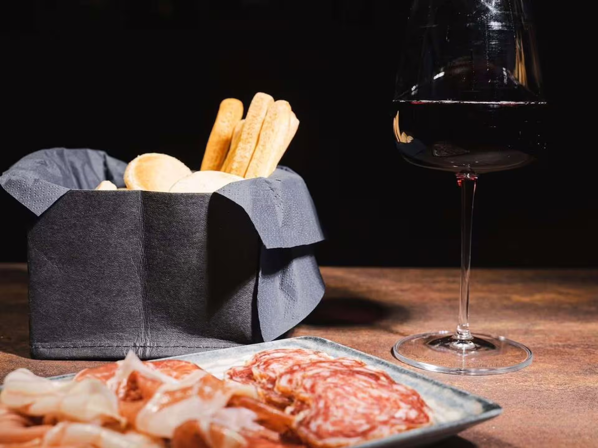 Red wine glass with cured meats and breadsticks, aperitivo pairing on luxury Modena city center wine tasting