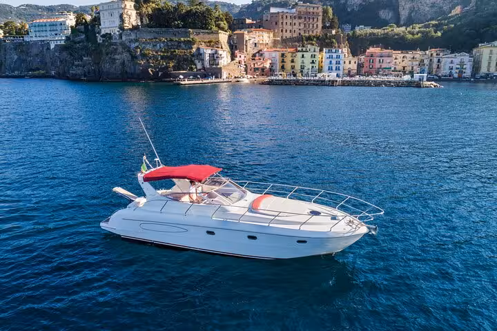 Elegant white yacht with a red canopy sails near Sorrento, offering a luxurious experience on the Italian coast.
