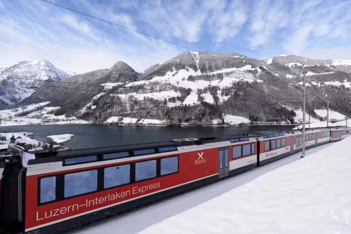Luzern-Interlaken Express glides through snowy Swiss mountains, offering breathtaking lake and alpine views.
