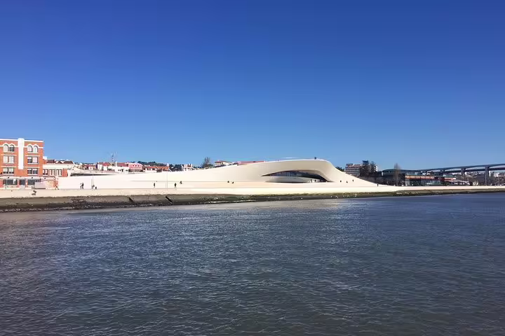 Modern architecture of MAAT museum along Lisbon's Tagus Riverbank under a bright blue sky.