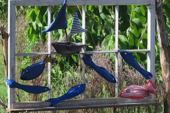 Colorful fabric fish and boats adorn a rustic frame against lush greenery, highlighting Madeira's artistic charm on a 4x4 adventure.