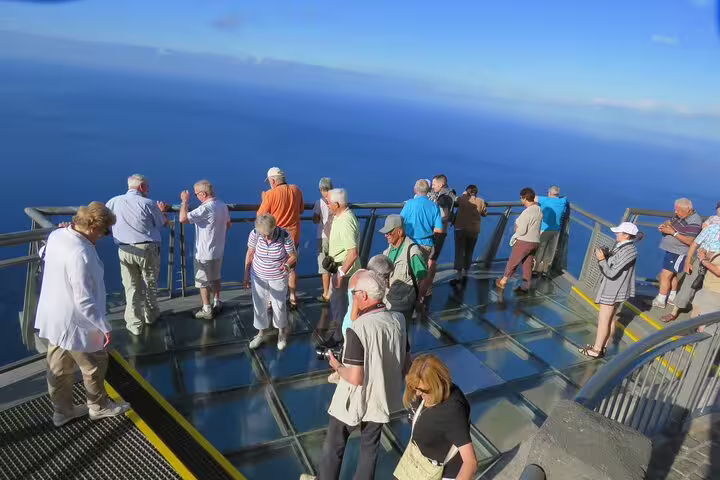 Tourists enjoy breathtaking ocean views from the glass-floored skywalk in Madeira during a guided 4x4 adventure with wine and tapas.