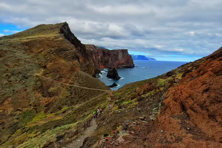 Scenic Madeira coastline with hikers on a rugged trail, showcasing the adventurous 4x4, hiking, swimming, and boat tour experience.