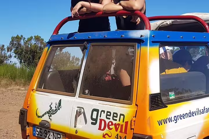 Two tourists enjoy a scenic view from a colorful off-road vehicle on a Madeira adventure tour with Skywalk and wine tasting.