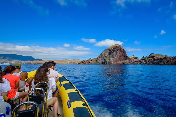Tourists enjoy a scenic boat ride in Madeira, surrounded by vibrant blue waters and breathtaking rocky landscapes.