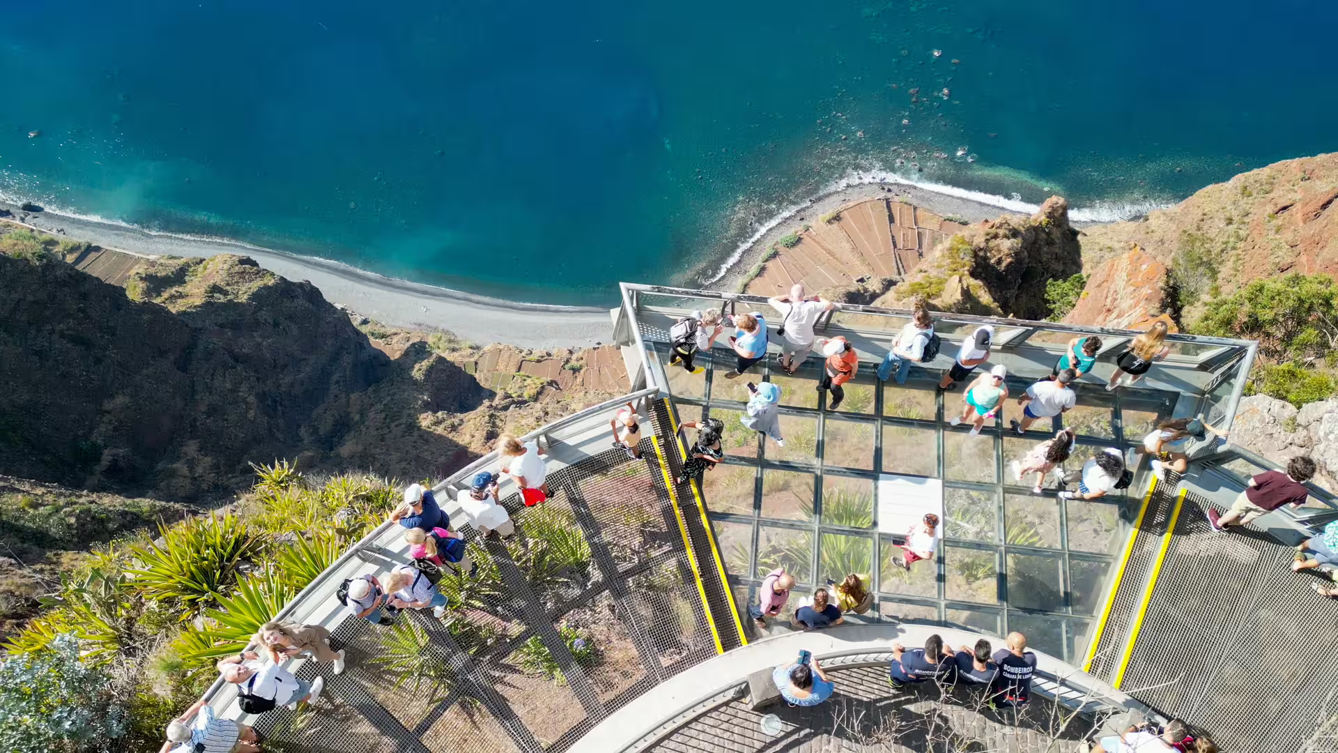 Aerial view of tourists enjoying the breathtaking glass skywalk at Cabo Girão, Madeira, with stunning ocean and cliff views.