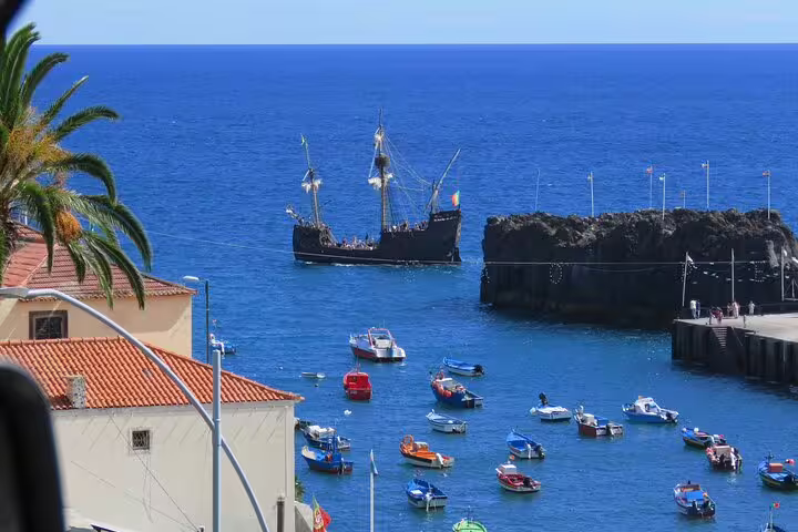 Colorful boats and a historic ship sail near the rocky coast of Madeira, highlighting its scenic ocean views and maritime charm.