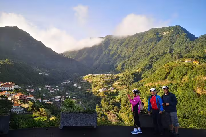 Cyclists enjoying a scenic e-bike tour on Madeira's lush North Coast, surrounded by verdant mountains and picturesque villages.