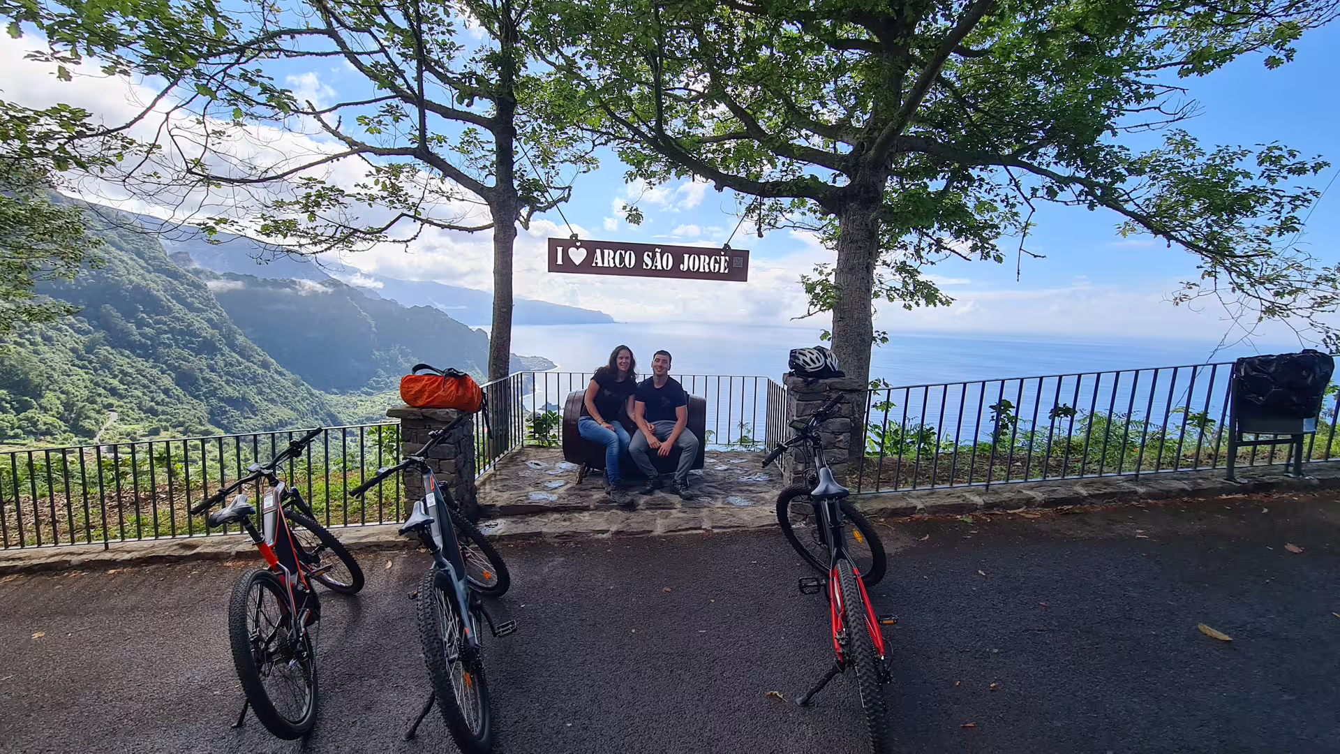 Couple enjoying Madeira's stunning North Coast view on a guided e-bike tour with scenic ocean and mountain backdrop.