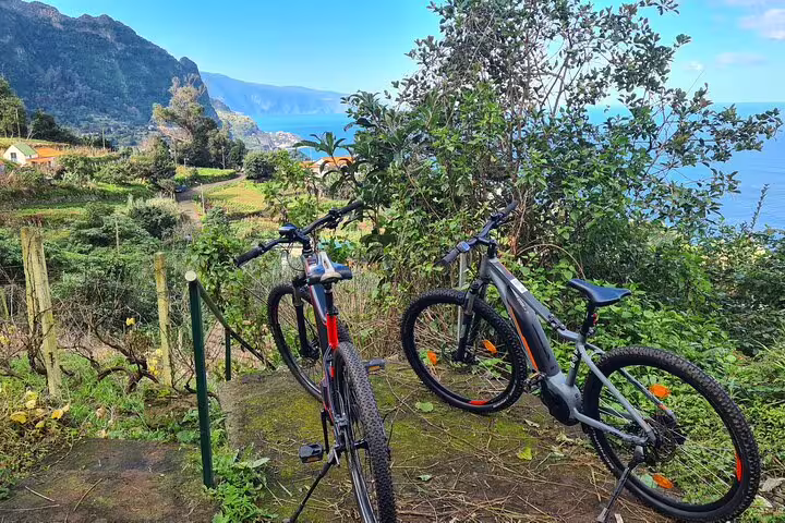 E-bikes parked along Madeira's scenic north coast trail with lush greenery and ocean views, perfect for guided tours.