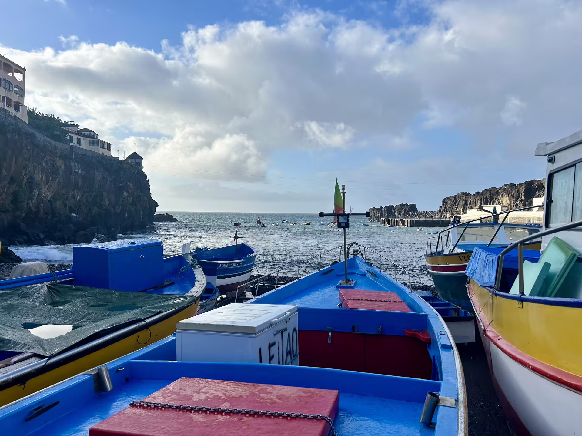 Colorful fishing boats docked by the scenic cliffs of Madeira, offering a glimpse of the island's vibrant coastal charm.