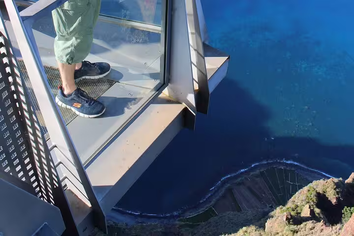 A person stands on a glass skywalk overlooking the ocean and cliffs in Madeira, part of a 4x4 adventure tour with wine and tapas.
