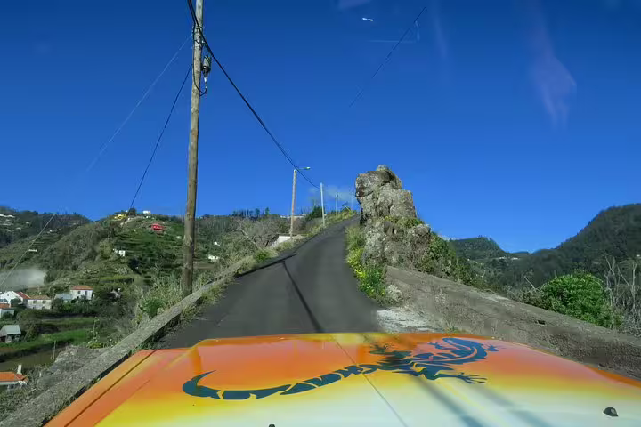 Scenic view from a vibrant tour vehicle navigating a narrow mountain road in Madeira, showcasing lush landscapes and clear skies.
