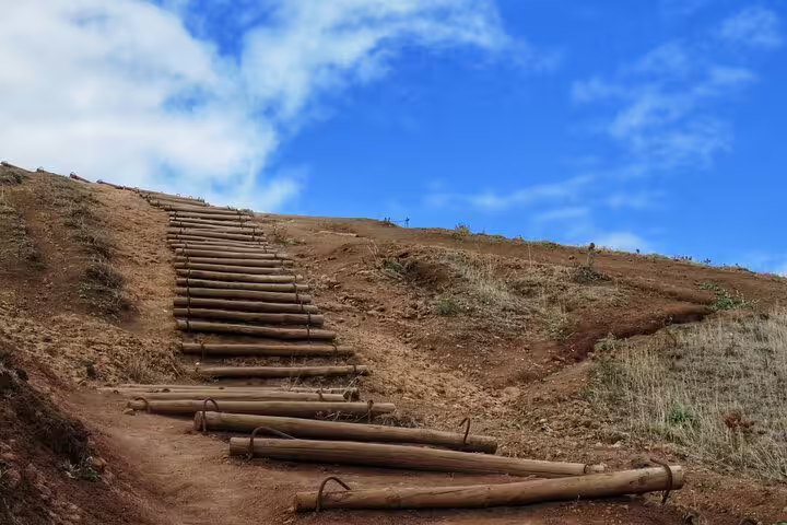 Wooden log steps leading up a dry hillside under a vibrant blue sky, showcasing the rugged terrain of Madeira's hiking trails.