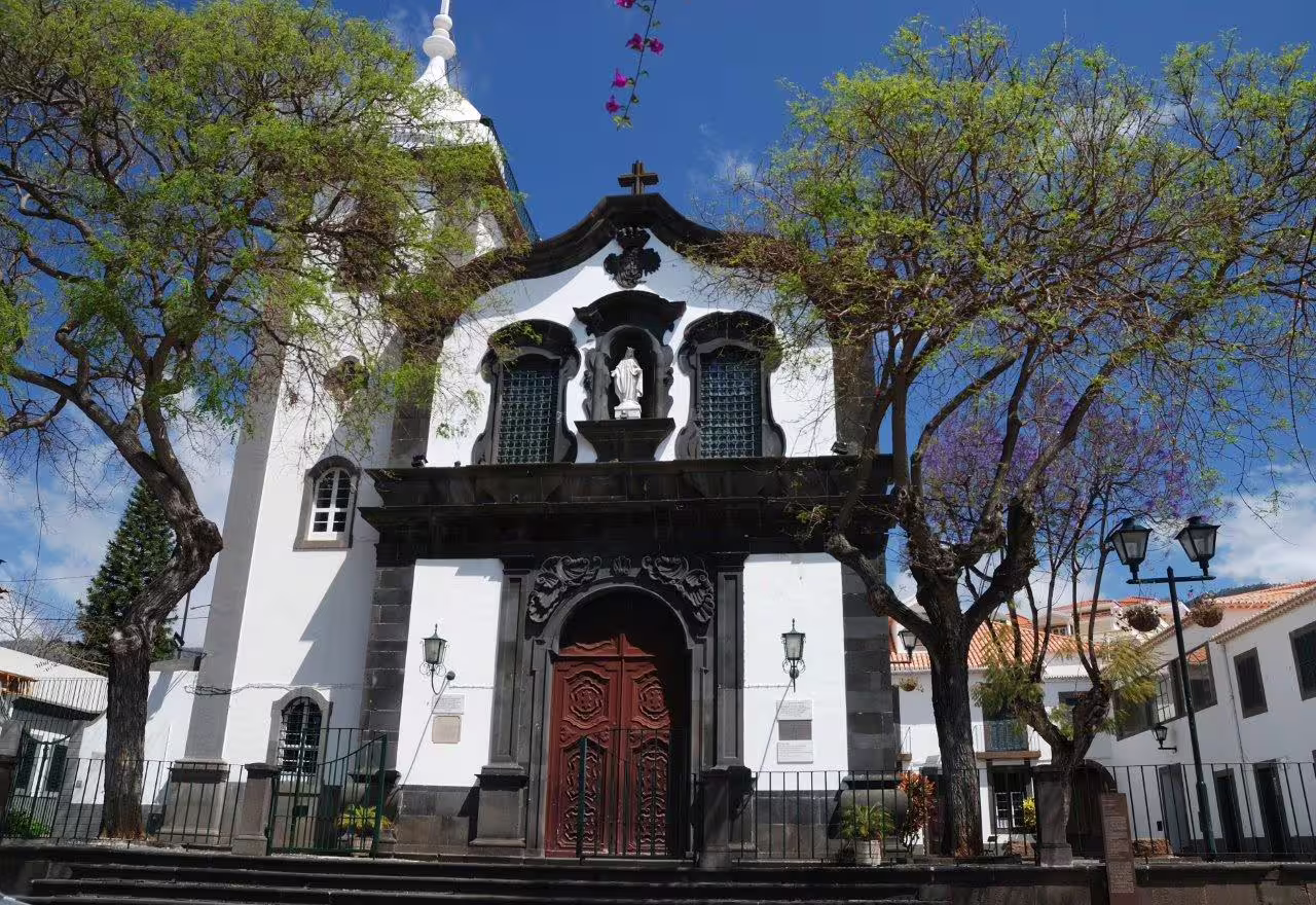 Historic church facade with ornate architecture and lush trees in Madeira, perfect for a scenic self-drive exploration.