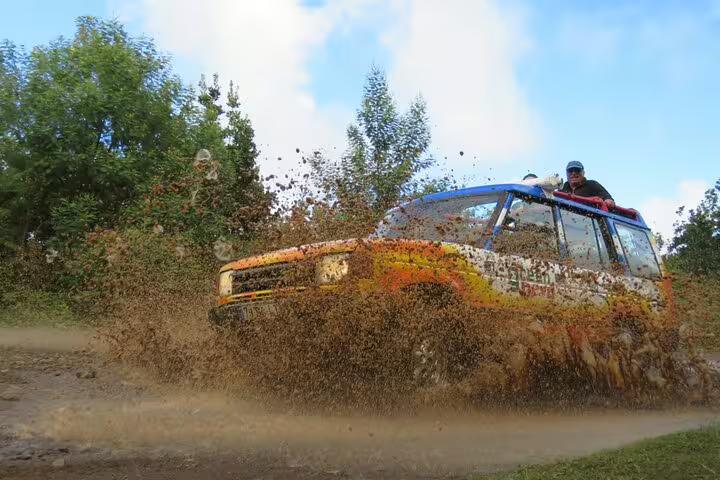 Adventurous 4x4 off-road experience in Madeira Islands, showcasing thrilling mud splashes amidst lush greenery on a guided tour.