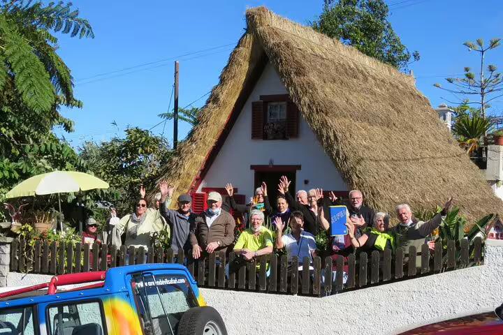 Tourists enjoying a sunny day at a traditional thatched house in Madeira, showcasing vibrant culture and scenic beauty.