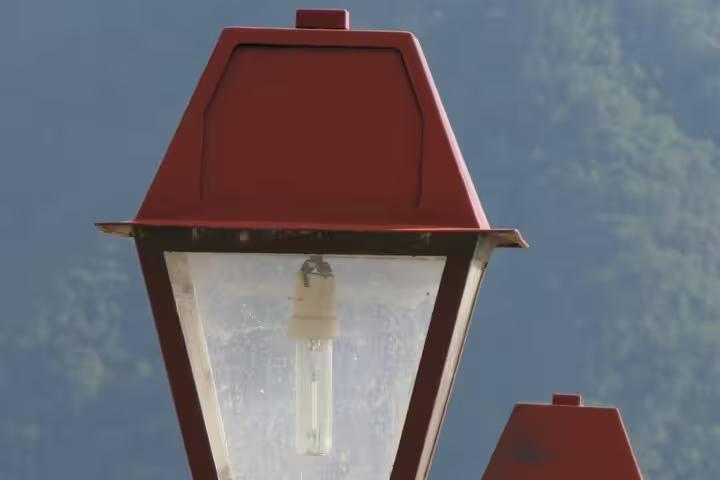 Close-up of a red vintage street lamp against the lush green backdrop of Madeira Islands, highlighting the charm of the guided tour.
