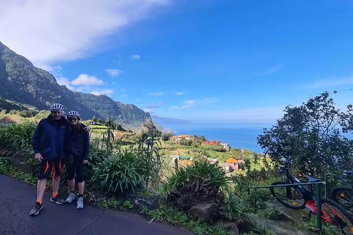 Cyclists enjoy a breathtaking view of Madeira's lush north coast during a guided e-bike tour under a clear blue sky.