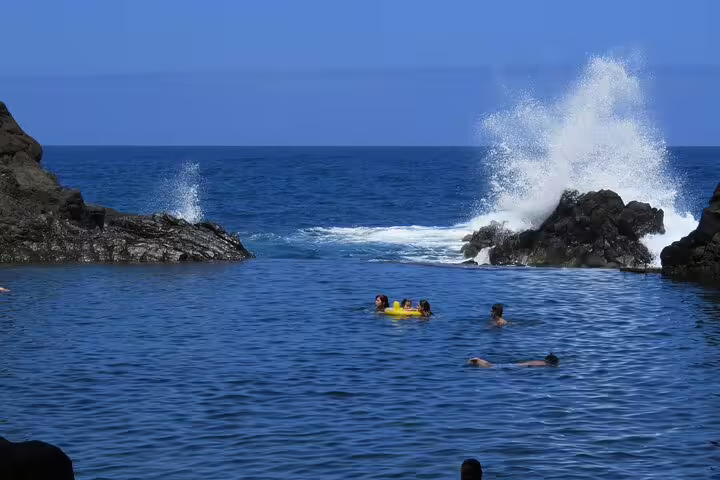 People swimming near rocky shores with waves crashing in the stunning blue waters of Madeira's northwest coast.