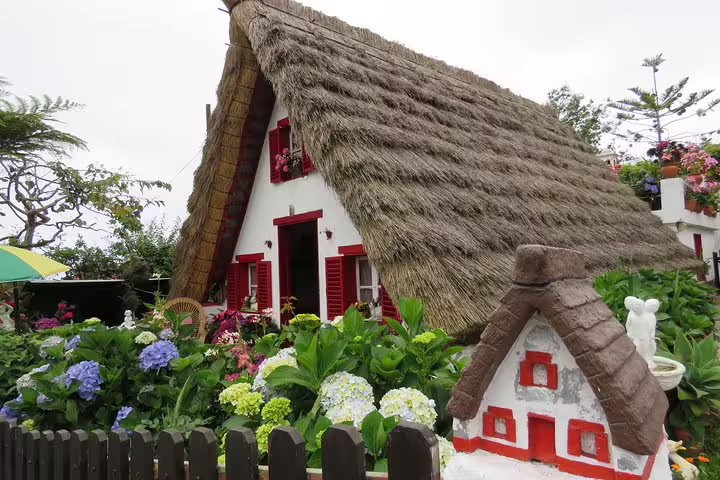 Traditional Santana house with thatched roof and colorful garden in Madeira, featured on the Madeira Peaks 4x4 Full-Day Tour.