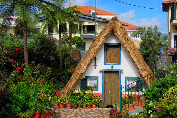 Charming traditional Santana house with a thatched roof surrounded by lush gardens, featured on Madeira Peaks 4X4 tour.