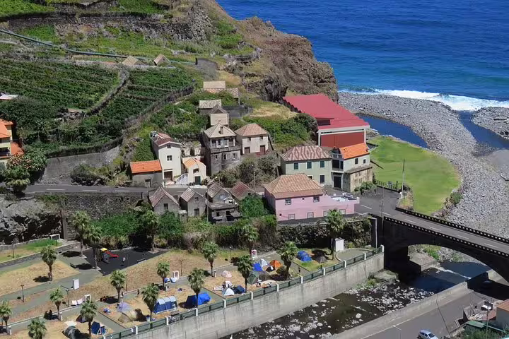 Aerial view of Madeira's coastal village with terraced vineyards, colorful houses, and ocean backdrop, ideal for jeep tour exploration.