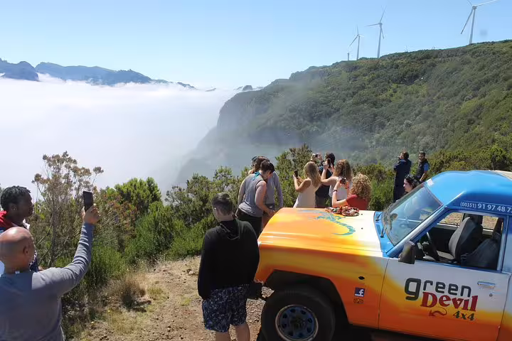 Tourists enjoy breathtaking views over Madeira's Enchanted Terraces on an open-top jeep tour, with lush landscapes and wind turbines.