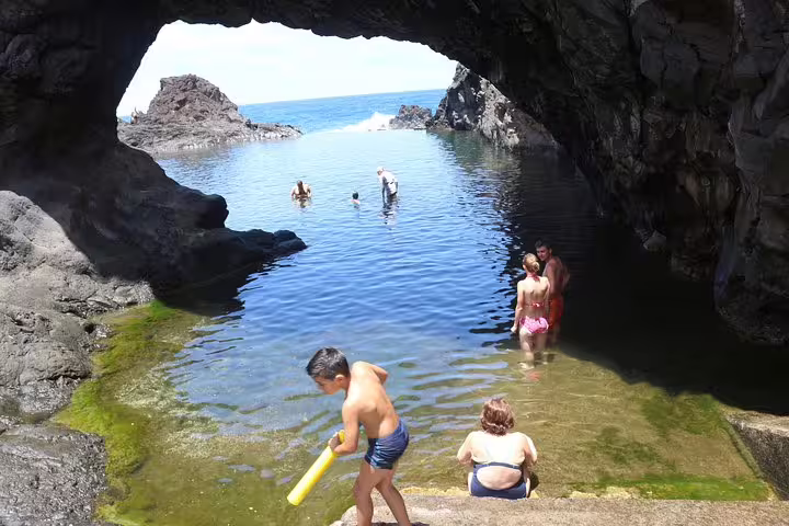 Family enjoying a swim in a natural rock pool under an arch in Madeira, showcasing the island's stunning coastal formations.