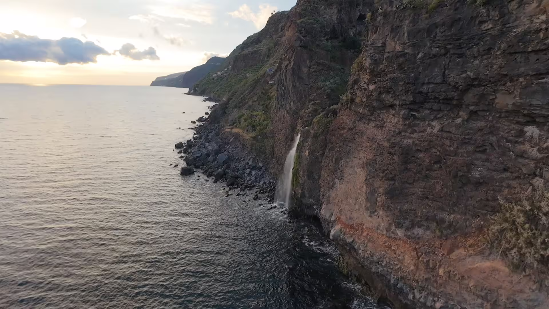 Scenic Madeira coastline with a stunning waterfall cascading into the ocean at sunset, perfect for a private, luxurious tour.