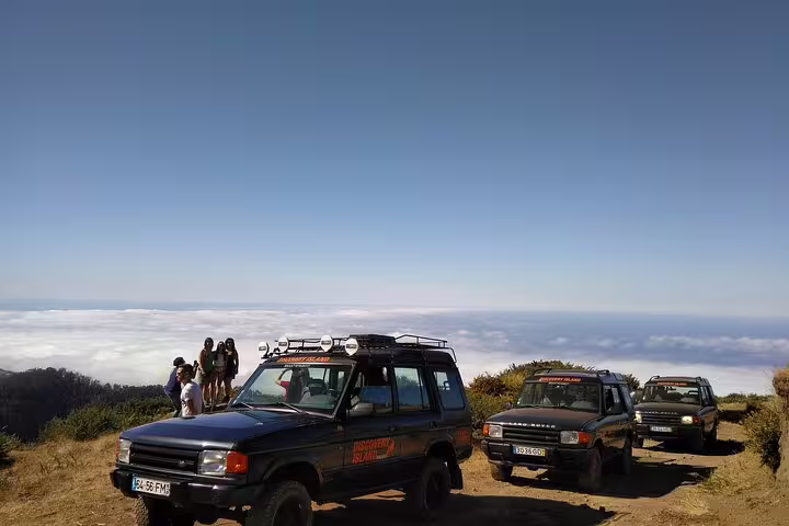 Safari jeeps and tourists on a Madeira mountain trail with breathtaking views of clouds and the island below.