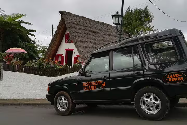 Traditional Santana house beside a Land Rover, highlighting cultural exploration on a Madeira Island tour.