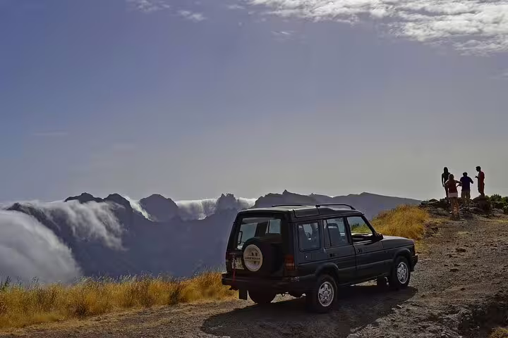 Tourists enjoying panoramic views of Madeira's western landscapes with a safari jeep parked nearby.
