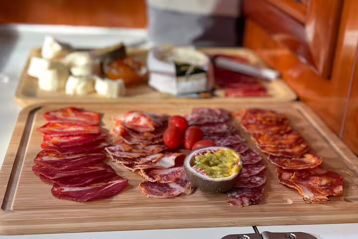 A delectable charcuterie board with assorted meats, cheeses, and tomatoes, offered during the Half Day Sailing Experience along Madeira's south coast.