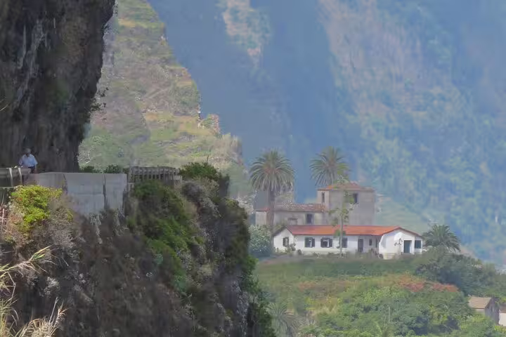 Stunning view of Madeira's lush cliffs and traditional houses on the Full Day Santana Wonders and Northeast 4WD Experience.
