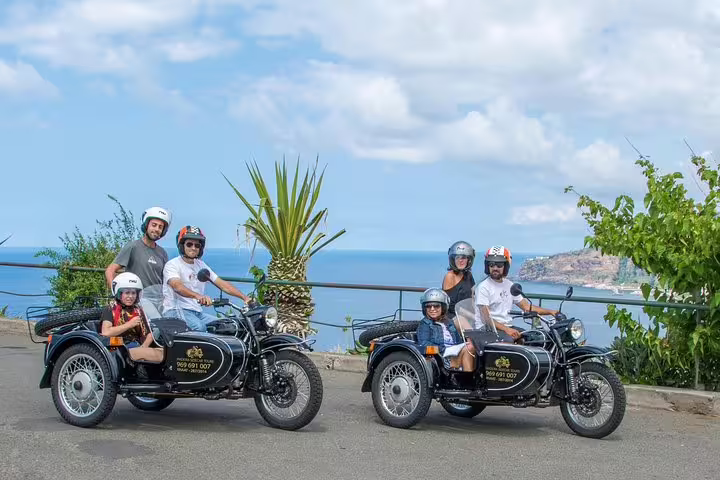 Families enjoying the scenic Madeira Old Road West sidecar tour with ocean views and lush greenery in the background.